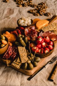 Delicious charcuterie board with meats, cheeses, crackers, and vegetables on a rustic linen backdrop.